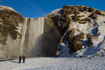 Tourists admire the Skogafoss waterfall in Iceland during the short winter day